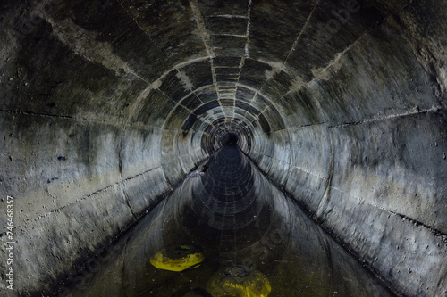 Flooded round underground drainage sewer tunnel reflecting in dirty sewage water