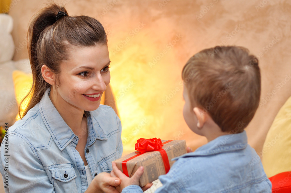 A little boy son gives a gift box with a red bow for his beloved mother. A little boy son gives a gift box with a red bow for his beloved mother.