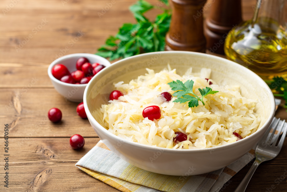 Sauerkraut with cranberries and parsley in bowl on wooden table. Selective focus. Sauerkraut with cranberries and parsley in bowl on wooden table. Selective focus.