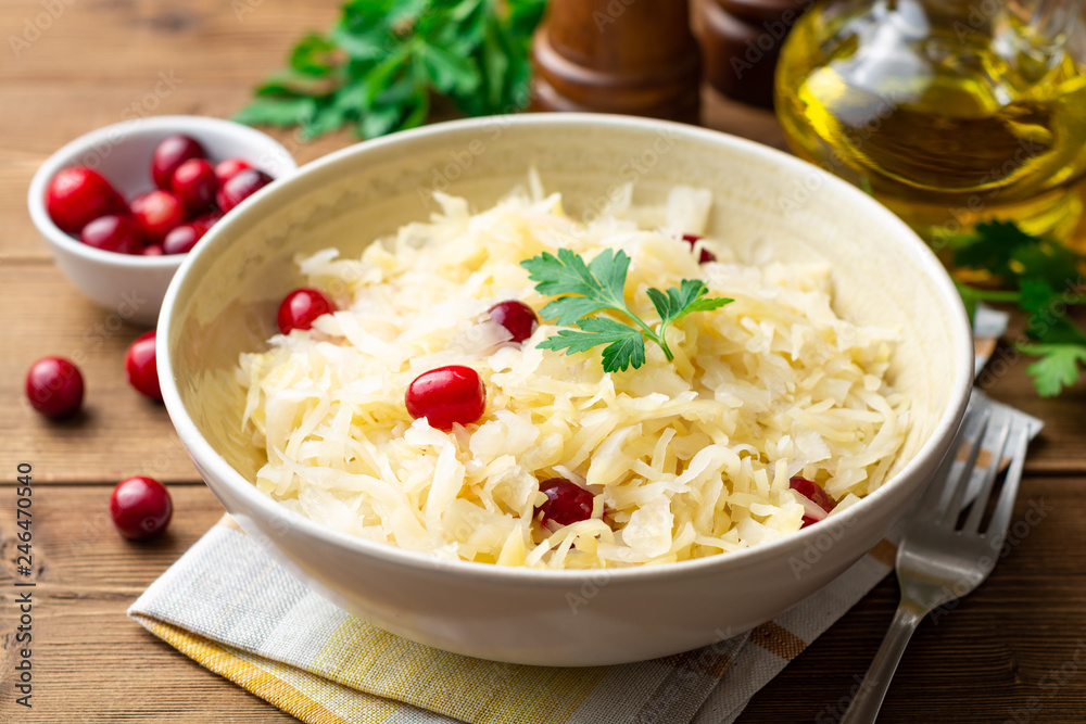 Sauerkraut with cranberries and parsley in bowl on wooden table. Selective focus. Sauerkraut with cranberries and parsley in bowl on wooden table. Selective focus.