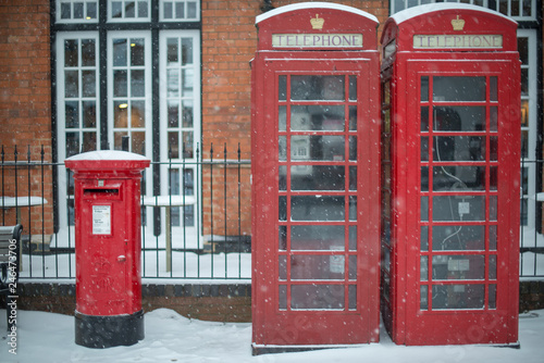 typical red post box and telephone kiosk on UK street during blizzard with snow on top