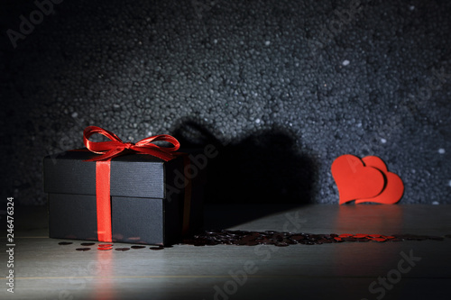 Czarne pudełko, prezent z czerwoną wstążką i sercem na deskach.