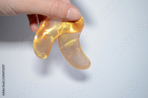 Transparent golden cosmetic eye patches holding in hand, on white background without face, with copyspace