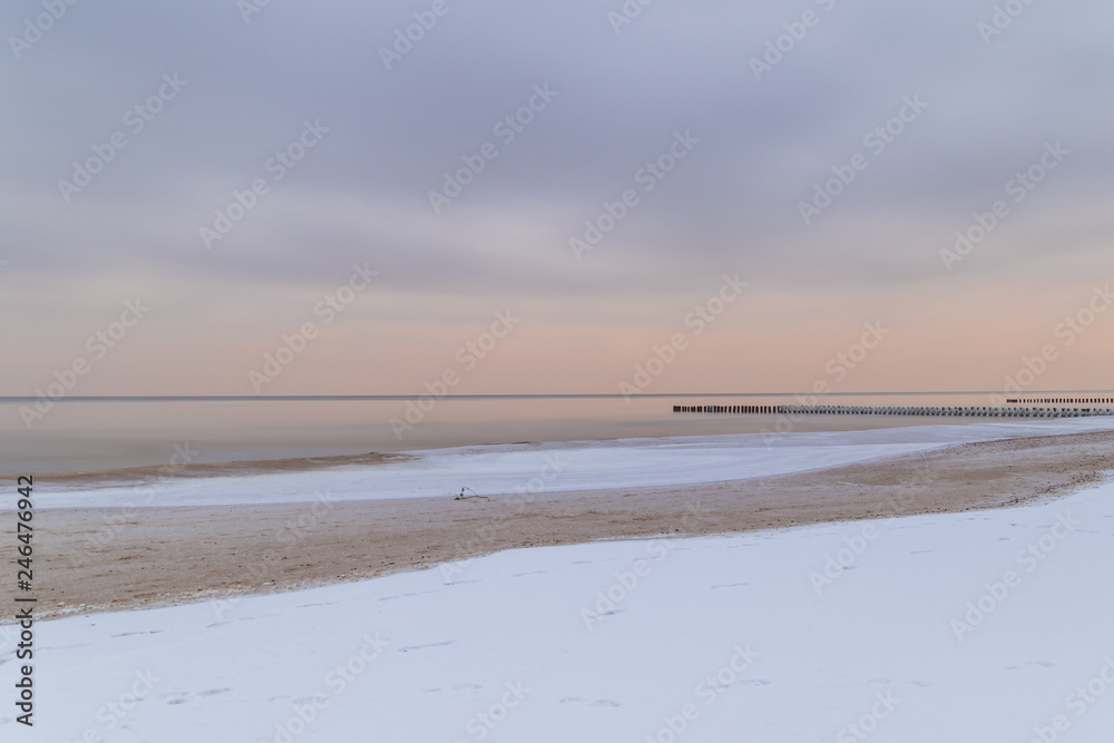 Winter landscape with snow on the beach on the Baltic sea coast at sunrise.