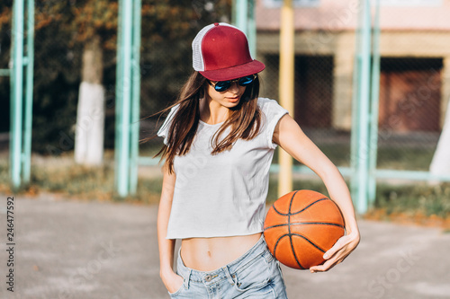Pretty young sporty girl with basketball ball outdoor.