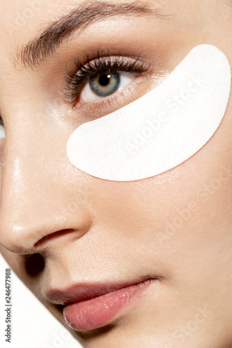 Fototapeta Close-up portrait of pensive pretty model taking care of skin with eye patches