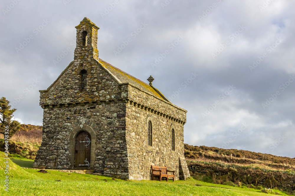 Non Chapel at Pembrokeshire coast an awe and small religious temple on the west coast of UK at Wales. The sunset rays illuminate the chapel stone walls with orange tones on a cloudy day