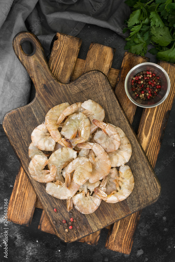 Fototapeta premium Raw tiger shrimp on the wood board on a dark background