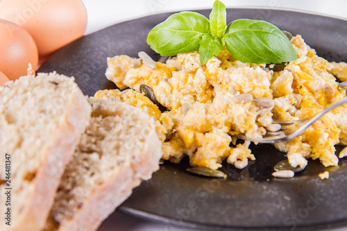 Scrambled eggs with sunflower and pumpkin seeds, some fresh eggs and wholemeal bread, eaten with a fork, decorated with basil, on a white background
