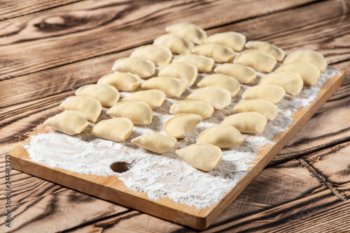 Raw dumplings on wooden cutting board, is ready to boil. Also known as Vareniks. Ukrainian traditional cuisine photo