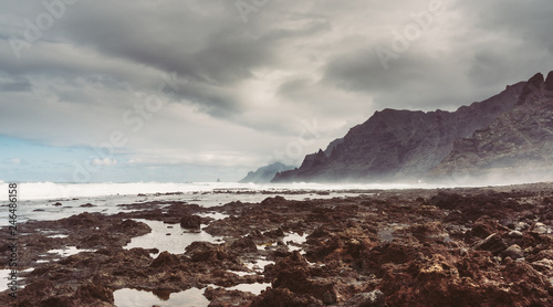 Punta del Hidalgo, Tenerife, Espania - October 27, 2018: Panorama of the rocky beach of Punta de Hidalgo and the waves breaking at the rocks, taken on a rainy day