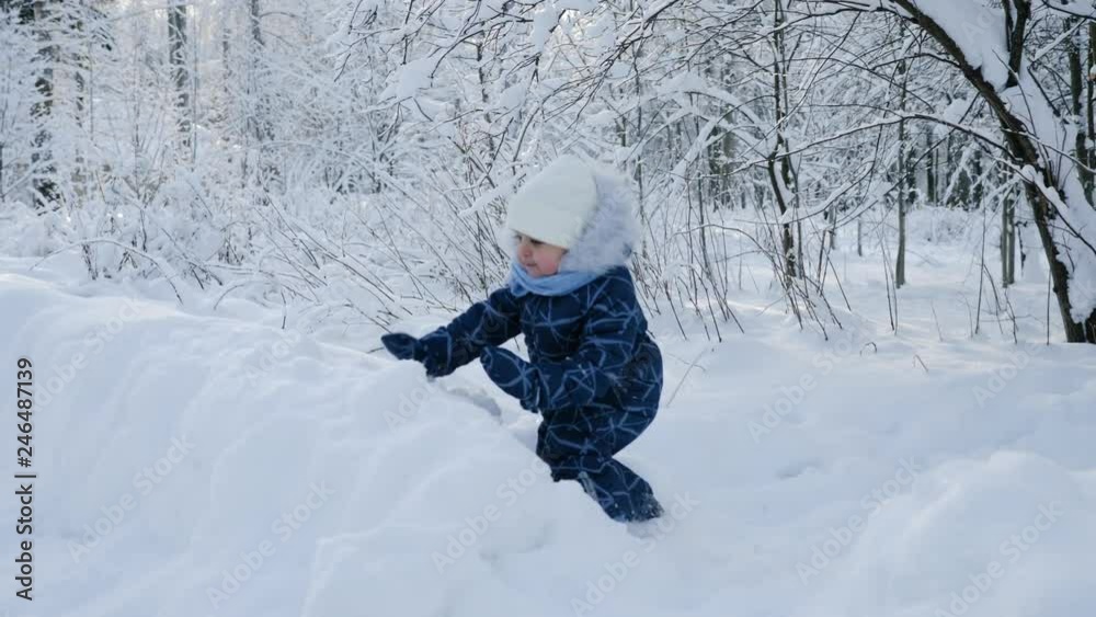 child sitting on the snow in the woods in the winter in a warm blue jumpsuit with fur child sitting on the snow in the woods in the winter in a warm blue jumpsuit with fur