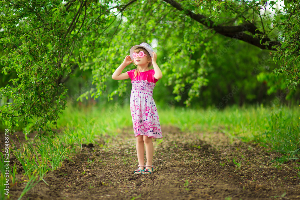 Happy ittle girl in bright dress and funny sunglasses walk in summer garden