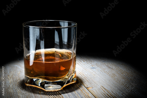 Glass of whiskey on a vintage wooden table on a black background.