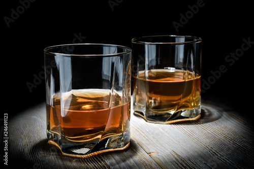 Two glasses of whiskey on a vintage wooden table on a black background.