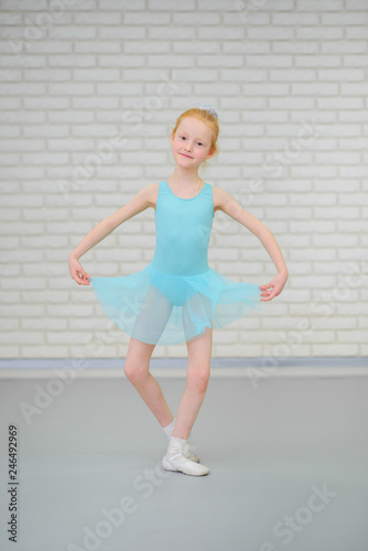 Cute little ballerina in blue dress dancing at ballet class.
