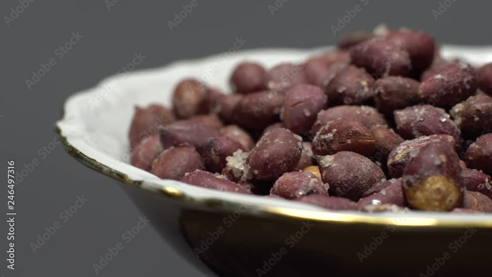 Raw unpeeled peanuts fried with salt. Rotation. Snack closeup. Peanuts in a bowl. Selective focus. grey background. Studio shot. Healthy food concept. Raw unpeeled peanuts fried with salt. Rotation. Snack closeup. Peanuts in a bowl. Selective focus. grey background. Studio shot. Healthy food concept.