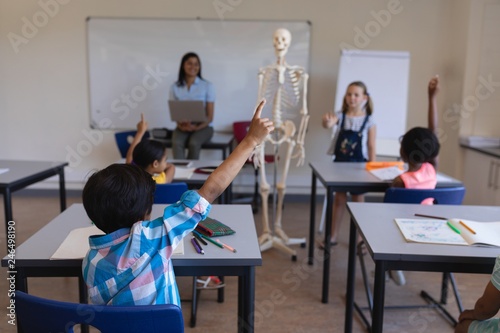 Schoolkids raising hands at desk in classroom