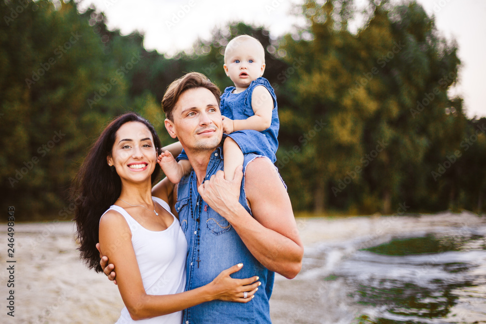 beautiful young family on vacation with baby. The father holds the blonde girl in her arms, and the brunette's mother hugs her husband. The concept of a family beach holiday summer near the sea beautiful young family on vacation with baby. The father holds the blonde girl in her arms, and the brunette's mother hugs her husband. The concept of a family beach holiday summer near the sea
