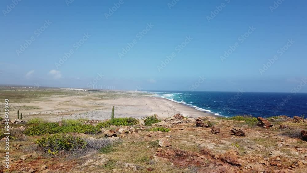 Aruba landscape including rocky terrain, beach and rough surf. There is a the turbines of a wind farm spinning in the background Aruba landscape including rocky terrain, beach and rough surf. There is a the turbines of a wind farm spinning in the background