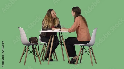 Two young women sitting at the table and talking. Green screen footage with alpha channel
