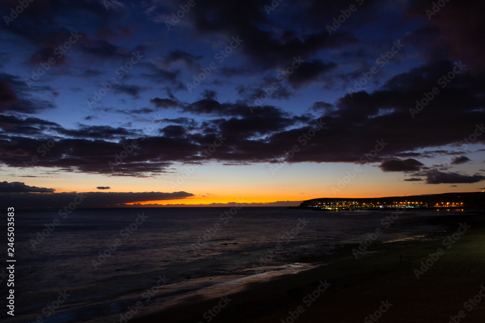 Fototapeta premium Dramatic cloudy sky at sunset in Meloneras beach, Gran Canaria. Fantastic twilight in Canary Islands, Spain. Night lights by the sea
