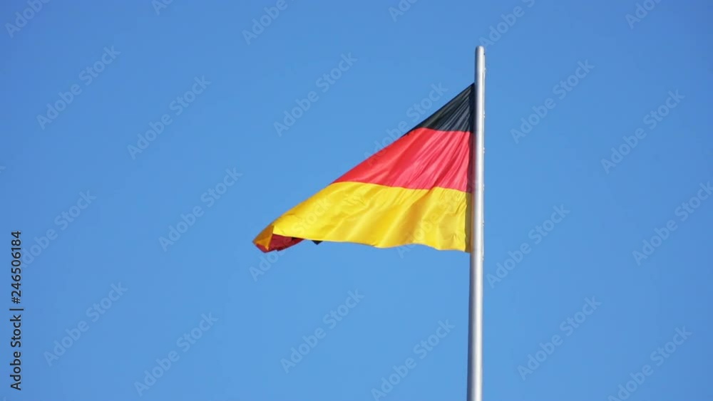 View of German national flag blowing in the wind on a clear sunny day. National flag of Germany on the mast against blue sky. View of German national flag blowing in the wind on a clear sunny day. National flag of Germany on the mast against blue sky.