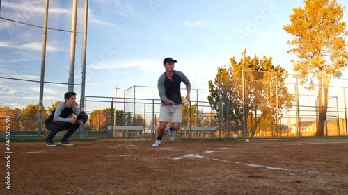 Amateur baseball player uses his bat to bit a bunt during a game on a public park field over home plate in spring time in America.