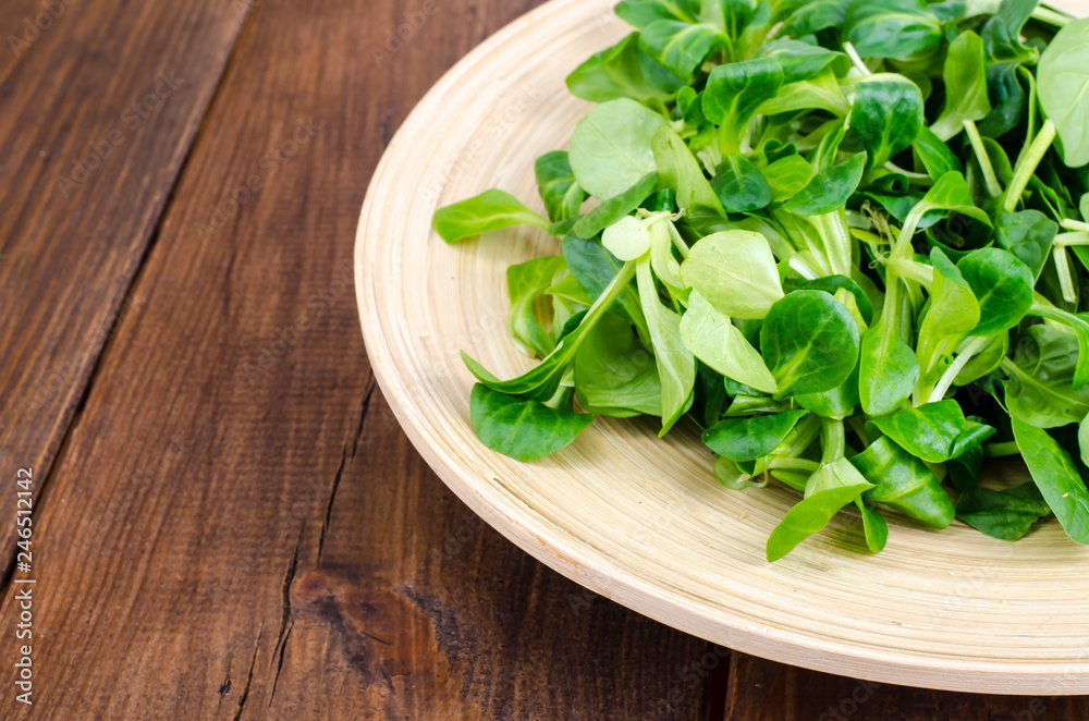 Mix of corn salad and spinach leaves on wooden plate Mix of corn salad and spinach leaves on wooden plate