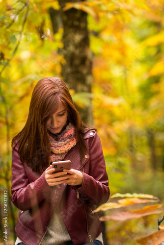 A young red-haired woman look at her mobile phone in the forest