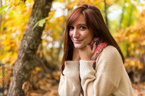 A young red-haired woman warming hands on her scarf in an autumnal forest  photo