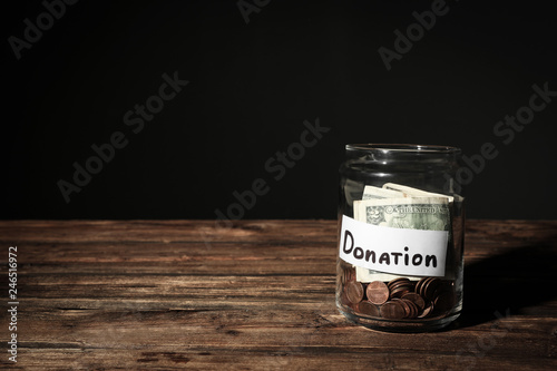 Glass jar with money and label DONATION on table against black background. Space for text