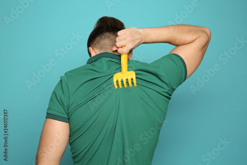 Young man scratching back with toy rake on color background. Annoying itch photo