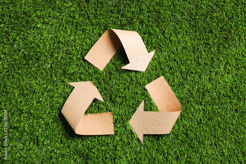 Fototapeta Recycling symbol cut out of kraft paper on green grass, top view