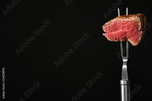 Carving fork with pieces of steak and space for text on black background. Tasty meat