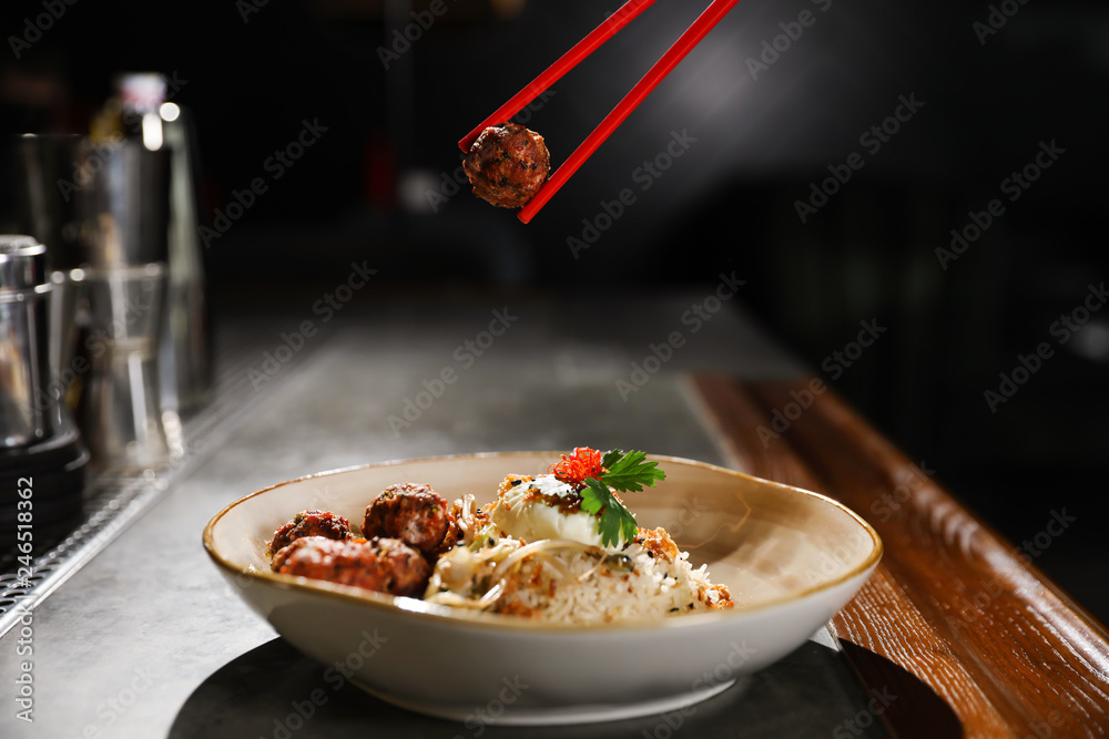 Chopsticks with meat ball over plate of rice on table indoors Chopsticks with meat ball over plate of rice on table indoors