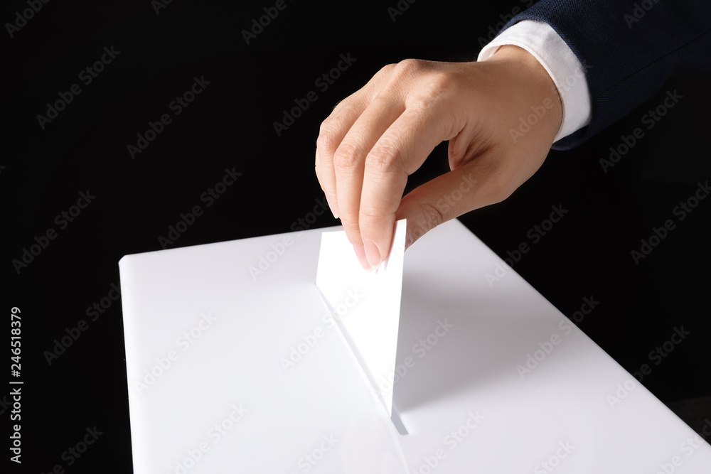 Woman putting her vote into ballot box on black background, closeup Woman putting her vote into ballot box on black background, closeup