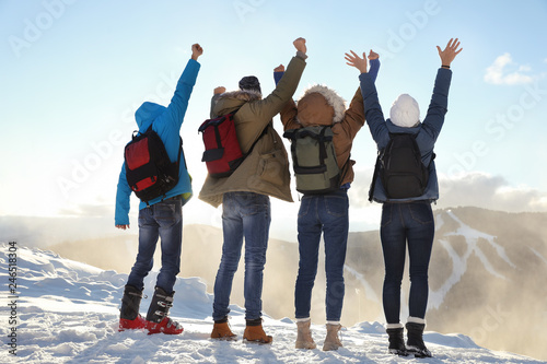 Group of excited friends with backpacks enjoying mountain view during winter vacation