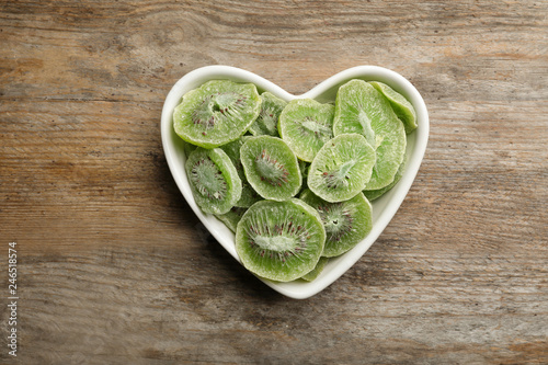 Bowl with slices of kiwi on wooden background, top view. Dried fruit as healthy food