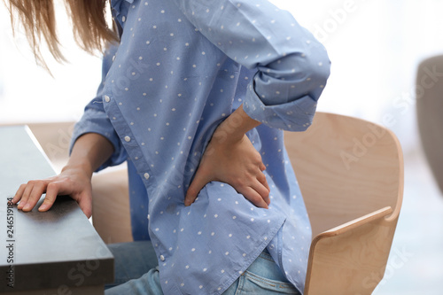 Young woman suffering from back pain in office, closeup