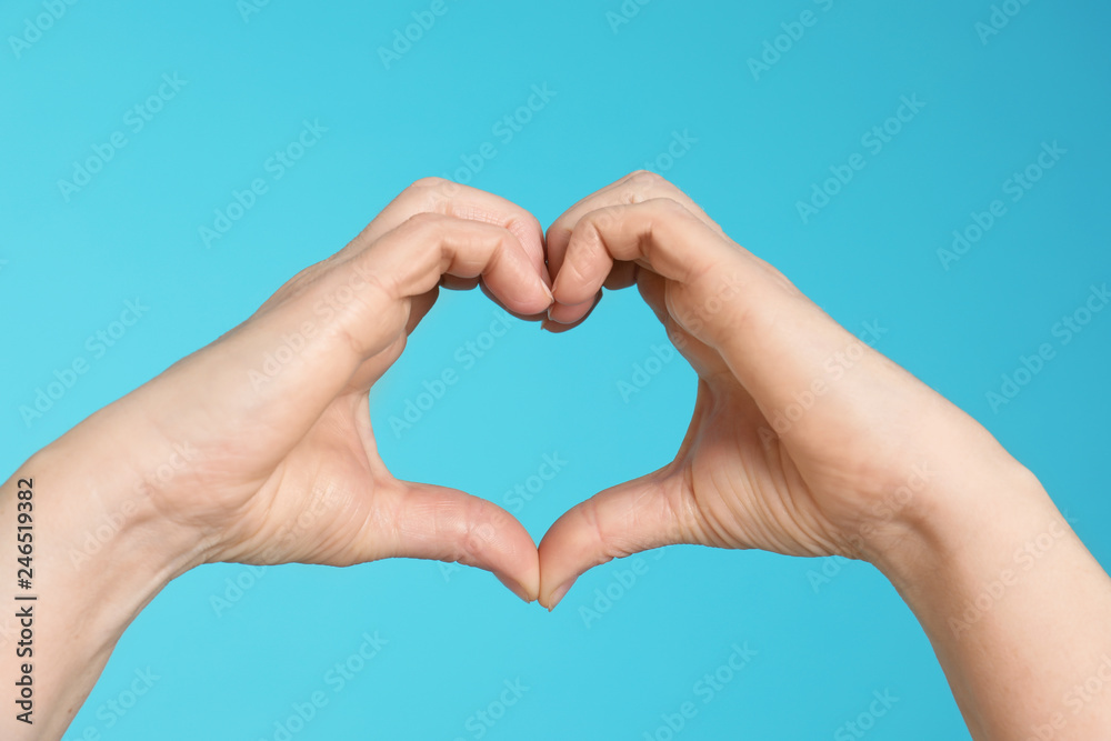 Woman making heart with her hands on color background, closeup Woman making heart with her hands on color background, closeup