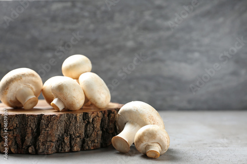 Fresh champignon mushrooms with wooden stump on table, space for text