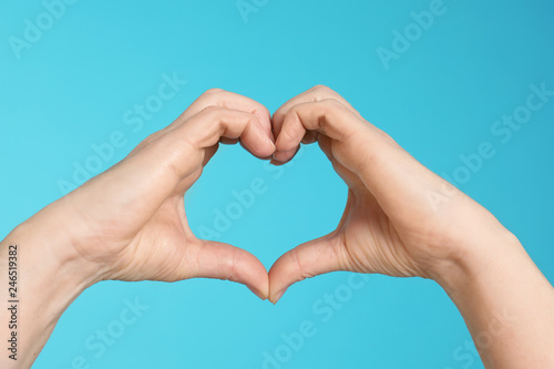 Woman making heart with her hands on color background, closeup