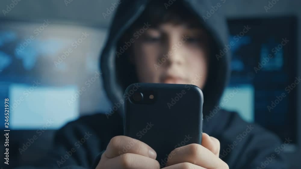 Young hooded boy using a smartphone device. Portrait of Genius boy wonder hacks system at cyberspace.
