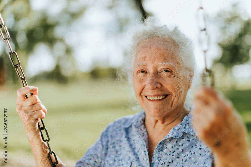 Cheerful senior woman on a swing at a playground - obrazy, fototapety, plakaty 