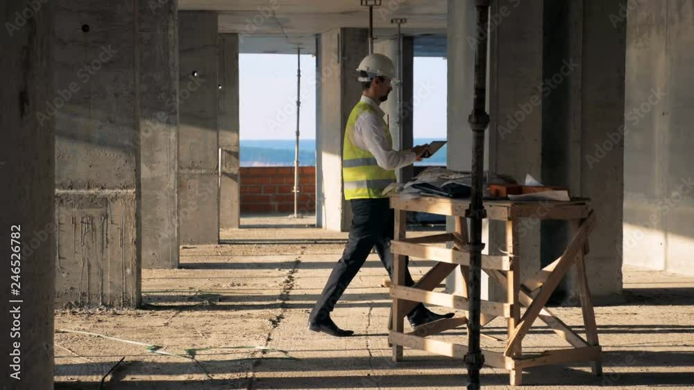 Male worker types on a tablet, walking in a building, side view.