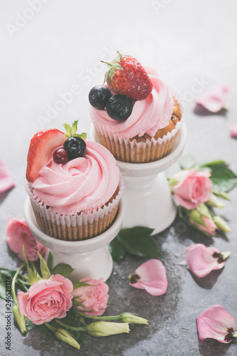 Cupcakes with on porcelain stands with rose flowers on a white background. Spring dessert concept with copy space