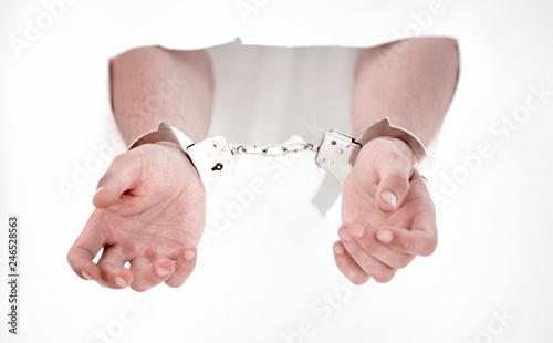 Handcuffs on the hands of a man breaking a paper wall