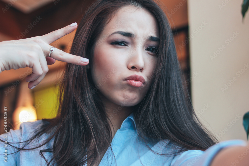 Fototapeta premium Beautiful charming brunette smiling asian girl taking selfie on frontal camera at cafe