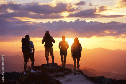 Group of four tourists or friends stands on mountain top and looks at sunset. Peoples travel concept